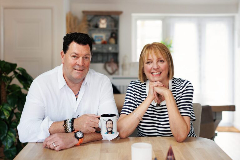 Andy and Jayne Porter sitting together at their kitchen table, Andy holding a mug printed with the Chen portrait