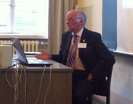 Dr Terence Palmer PhD seated at a laptop, presenting his research to a conference audience