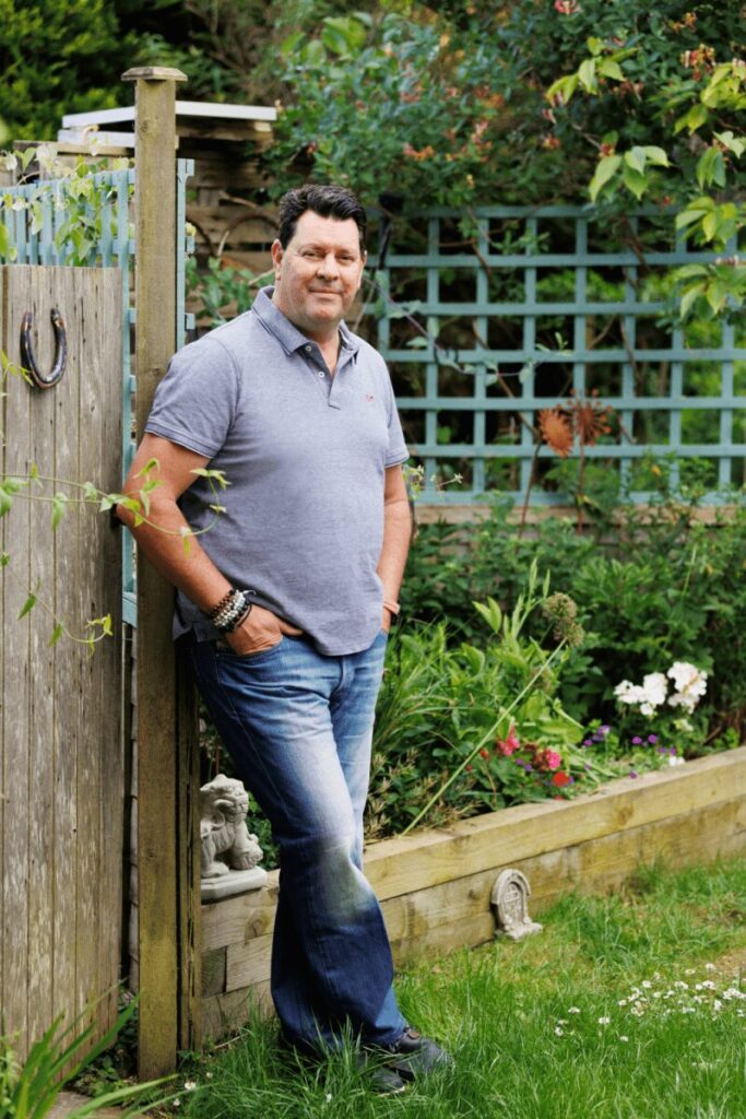 Andy Porter standing in his garden, leaning on a wooden fence