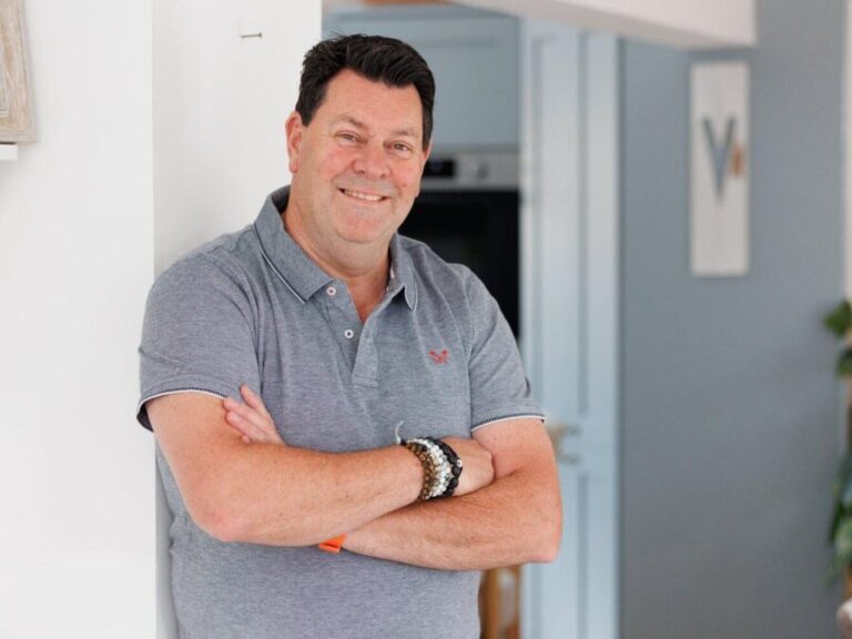 Andy Porter standing in a kitchen doorway with his arms folded, smiling at the camera