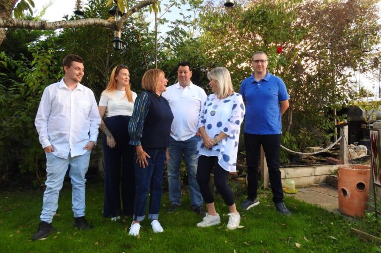 The team standing together in a garden, laughing, with trees and bird feeders behind them
