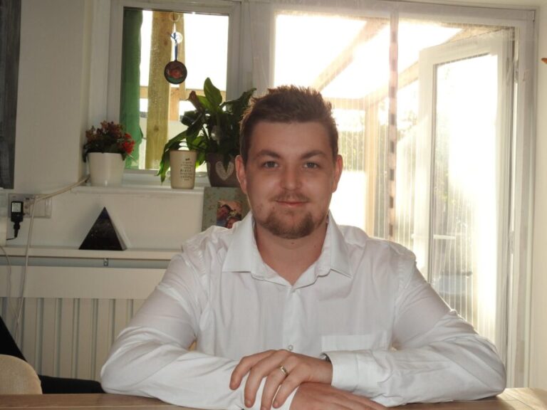 Oliver Porter sitting at a table in a white shirt, smiling at the camera