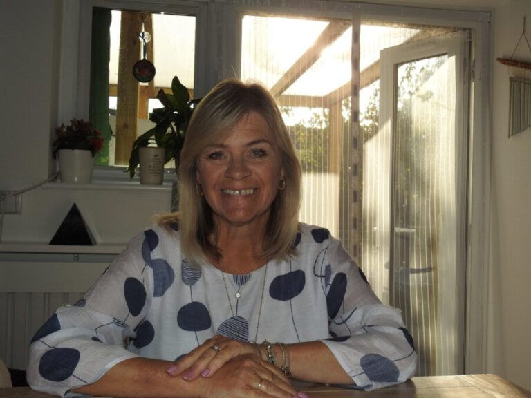 Vanessa Burton sitting at a table in a patterned blue and white top, smiling at the camera